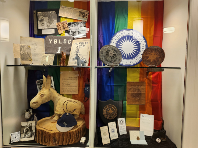 A picture showing the various Colby seals, memorabilia, and a carved Mule with a rainbow backdrop in the cases.
