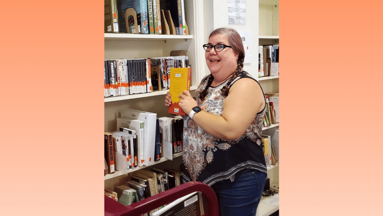Robin standing next to a course reserve books and holding one.