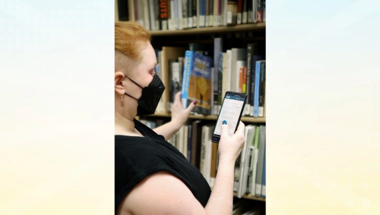 A library worker uses thier phone to look up a book from the stacks.