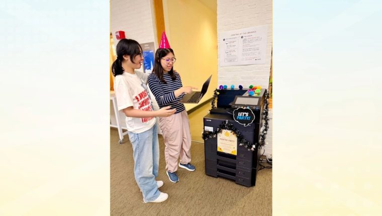 Two students in party hats connect to the library printer